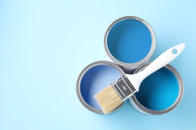 Image of Cans with paint in shades of blue and brush on color background, top view. Space for text
