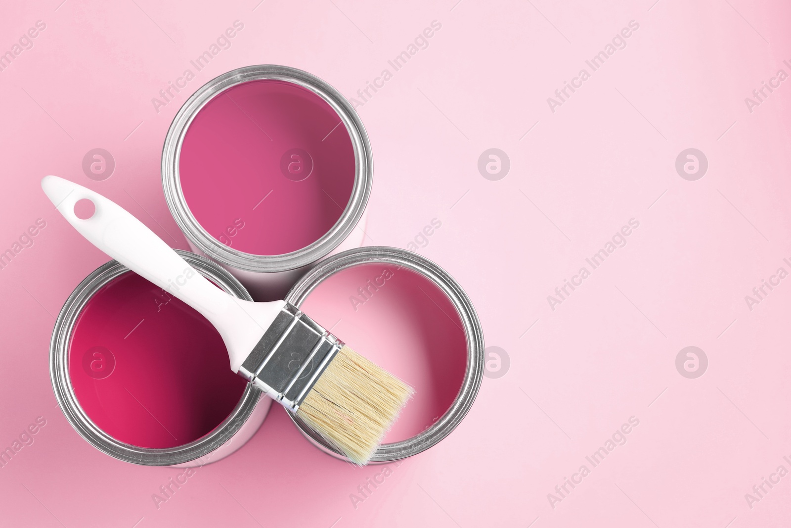 Cans with paint in shades of pink and brush on color background, top view. Space for text Image of Cans with paint in shades of pink and brush on color background, top view. Space for text