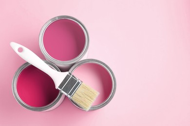 Image of Cans with paint in shades of pink and brush on color background, top view. Space for text