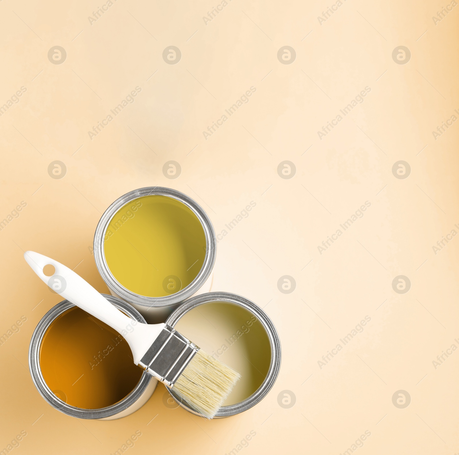 Cans with paint in shades of yellow and brush on beige background, top view. Space for text Image of Cans with paint in shades of yellow and brush on beige background, top view. Space for text