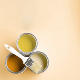 Image of Cans with paint in shades of yellow and brush on beige background, top view. Space for text