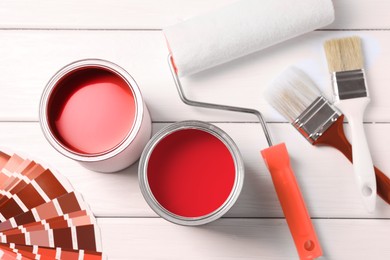Image of Cans with paint in shades of red, color palette, roller and brushes on white wooden background, top view