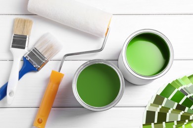 Image of Cans with paint in shades of green, color palette, roller and brushes on white wooden background, top view