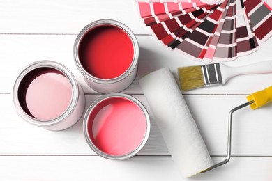 Image of Cans with paint in shades of red, color palette, roller and brush on white wooden background, top view