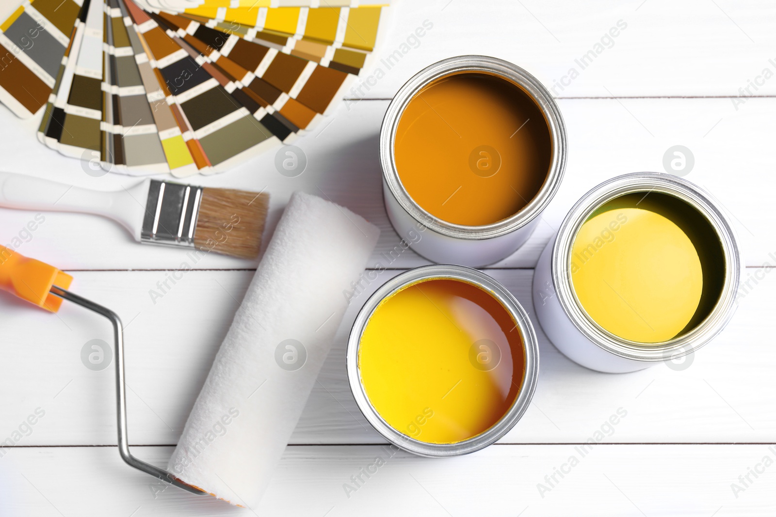 Cans with paint in shades of yellow, color palette, roller and brush on white wooden background, top view Image of Cans with paint in shades of yellow, color palette, roller and brush on white wooden background, top view