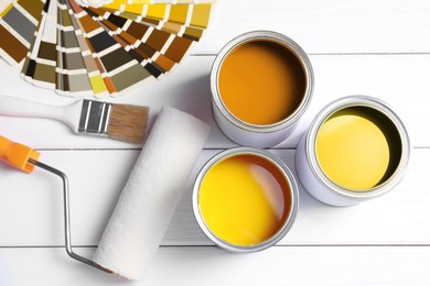 Image of Cans with paint in shades of yellow, color palette, roller and brush on white wooden background, top view