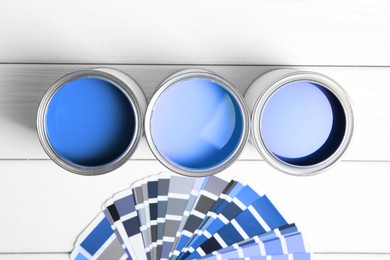 Image of Cans with paint in shades of blue and color palette on white wooden background, top view