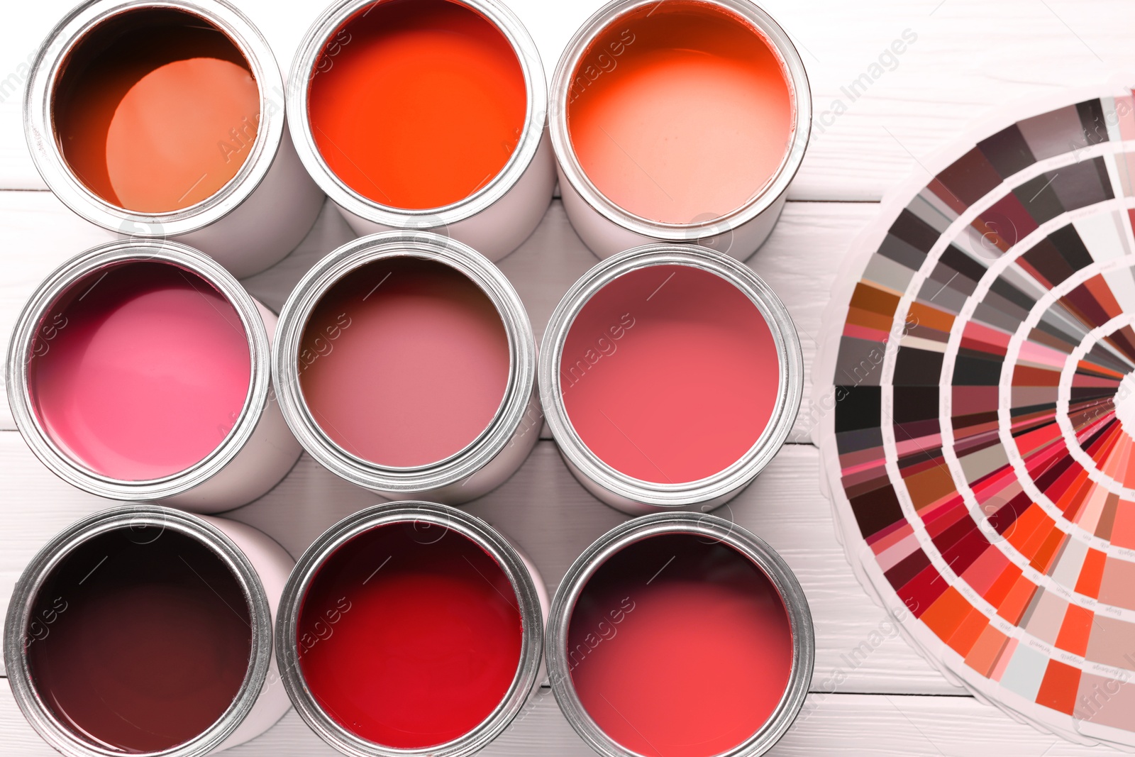 Cans with paint in shades of red and color palette on white wooden background, top view Image of Cans with paint in shades of red and color palette on white wooden background, top view