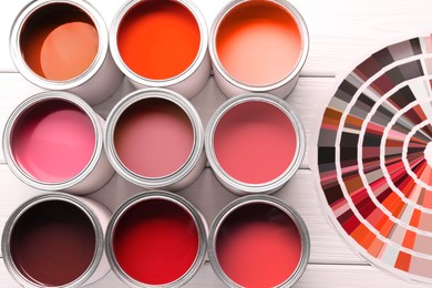 Image of Cans with paint in shades of red and color palette on white wooden background, top view