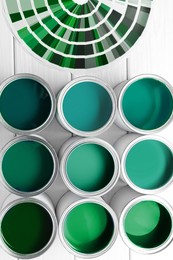 Image of Cans with paint in shades of green and color palette on white wooden background, top view
