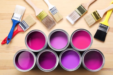 Image of Cans with paint in shades of violet and brushes on wooden background, top view