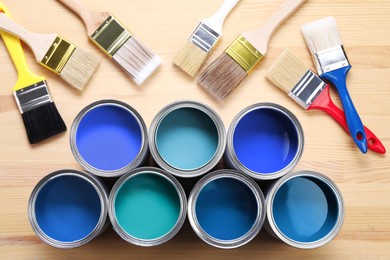 Image of Cans with paint in shades of blue and brushes on wooden background, top view