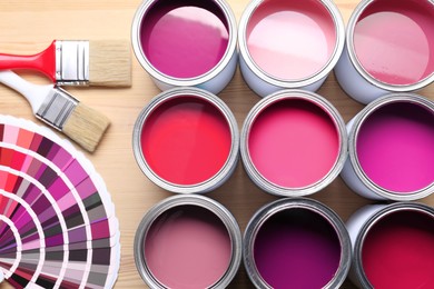Image of Cans with paint in shades of pink, color palette and brushes on wooden background, top view