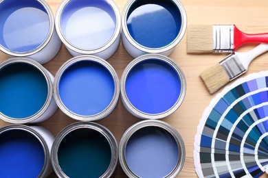 Image of Cans with paint in shades of blue, color palette and brushes on wooden background, top view