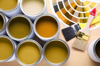 Image of Cans with paint in shades of yellow, color palette and brushes on wooden background, top view