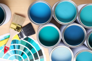 Image of Cans with paint in shades of blue, color palette and brushes on wooden background, top view