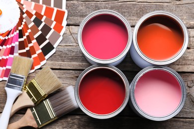 Image of Cans with paint in shades of red, color palette and brushes on wooden background, top view