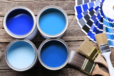 Image of Cans with paint in shades of blue, color palette and brushes on wooden background, top view