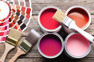Image of Cans with paint in shades of red, color palette and brushes on wooden background, top view