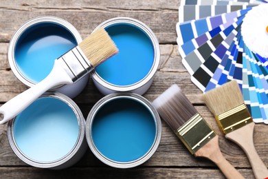 Image of Cans with paint in shades of blue, color palette and brushes on wooden background, top view