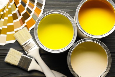 Image of Cans with paint in shades of yellow, color palette and brushes on wooden background, top view