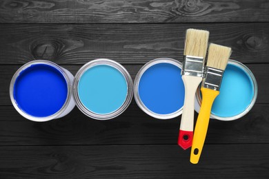 Image of Cans with paint in shades of blue and brushes on black wooden background, top view