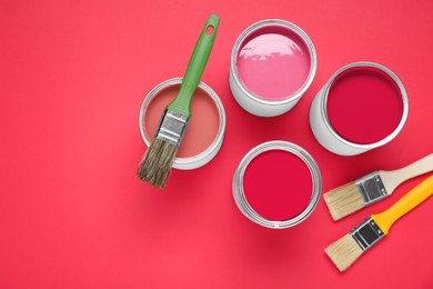 Image of Cans with paint in shades of red and brushes on color background, top view