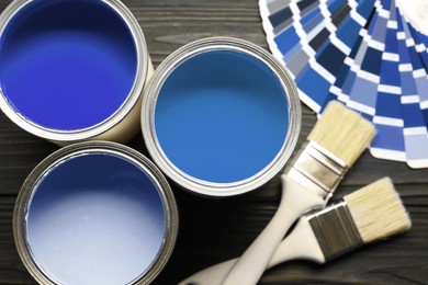 Image of Cans with paint in shades of blue, color palette and brushes on wooden background, top view