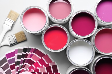 Image of Cans with paint in different shades, brushes and color palette on white background, top view