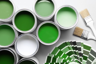 Image of Cans with paint in different shades, brushes and color palette on white background, top view