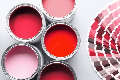 Image of Cans with paint in shades of red and color palette on white background, top view