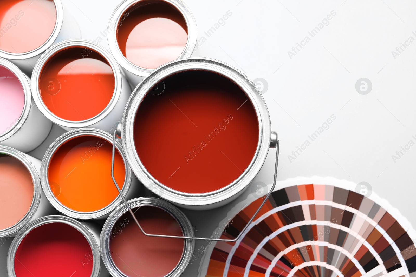 Cans with paint in shades of red and color palette on white background, top view Image of Cans with paint in shades of red and color palette on white background, top view