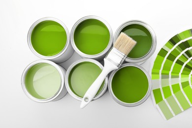 Image of Cans with paint in shades of green, brush and color palette on white background, top view