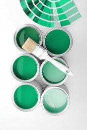 Image of Cans with paint in shades of green, brush and color palette on white background, top view