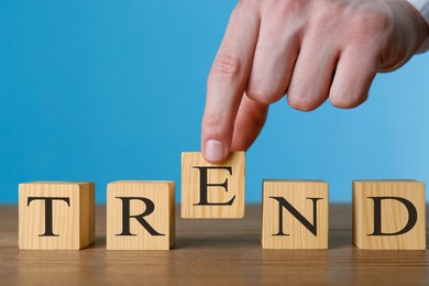 Image of Man making word Trend with wooden cubes at table against blue background, closeup