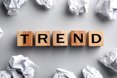 Image of Word Trend made of wooden cubes with letters and crumpled paper balls on light grey background, top view
