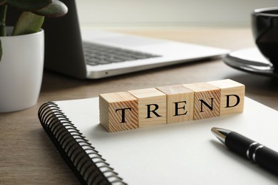 Image of Word Trend made of wooden cubes on notebook. Workplace with stationery and laptop on table