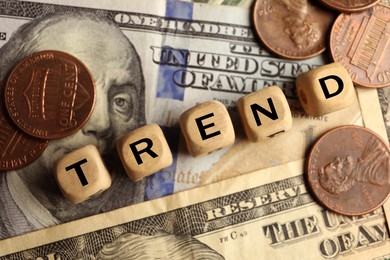 Image of Word Trend made of wooden cubes with letters and coins on dollar bills, top view