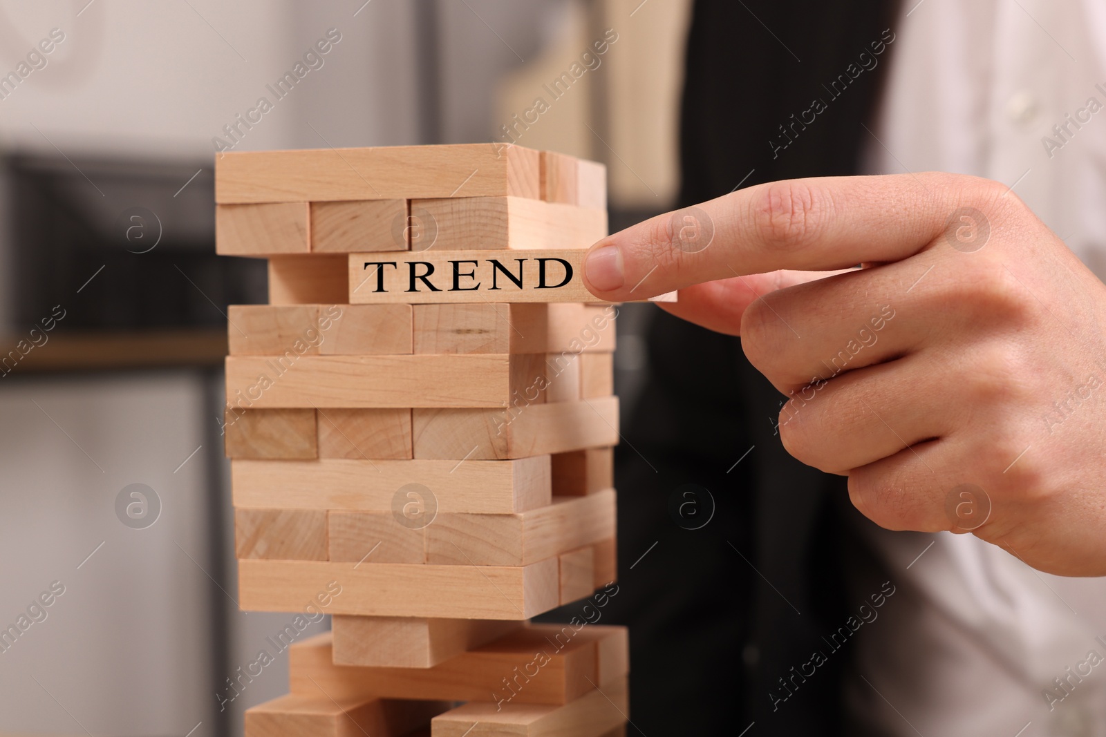 Man removing wooden block with word Trend from tower indoors, closeup Image of Man removing wooden block with word Trend from tower indoors, closeup
