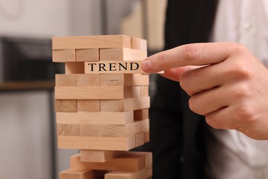 Image of Man removing wooden block with word Trend from tower indoors, closeup