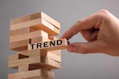 Image of Man removing wooden block with word Trend from tower on grey background, closeup