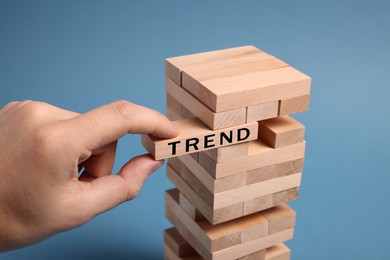 Image of Man removing wooden block with word Trend from tower on blue background, closeup