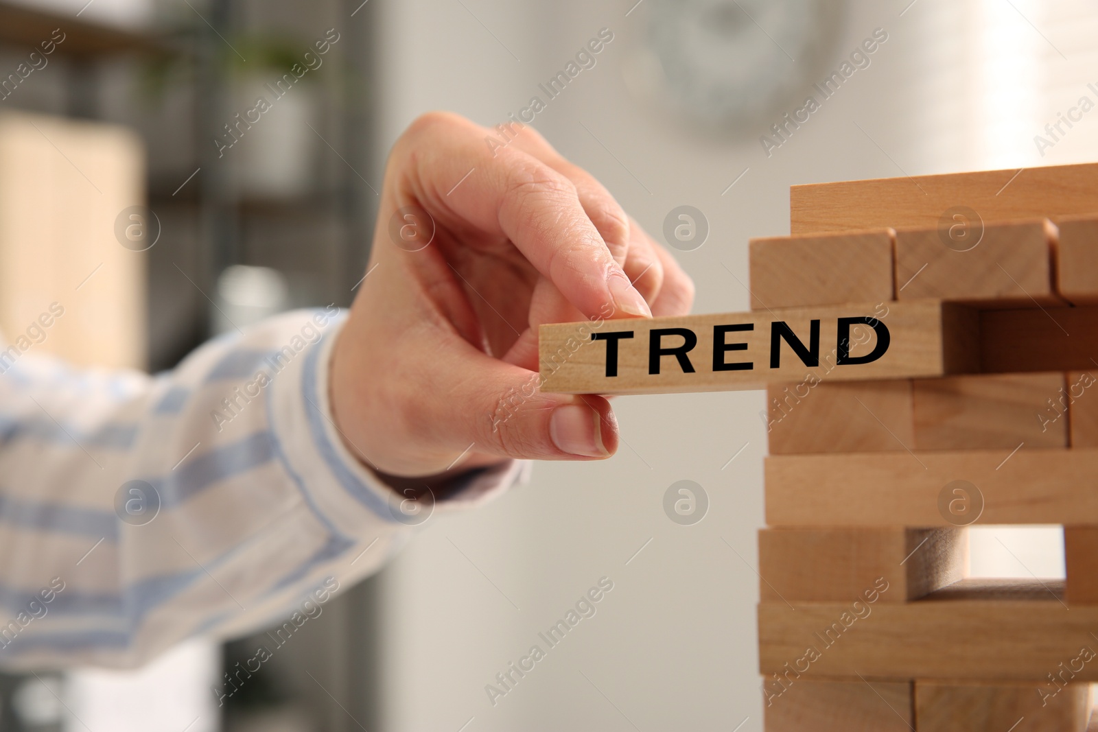 Woman removing wooden block with word Trend from tower indoors, closeup Image of Woman removing wooden block with word Trend from tower indoors, closeup