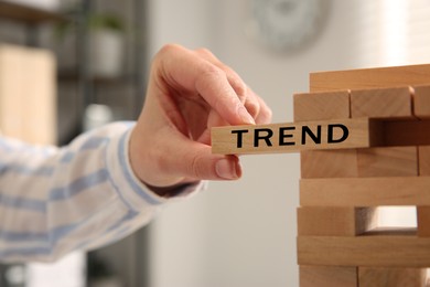 Image of Woman removing wooden block with word Trend from tower indoors, closeup