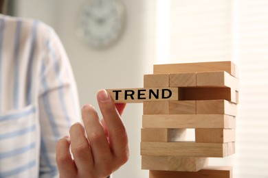 Image of Woman removing wooden block with word Trend from tower indoors, closeup