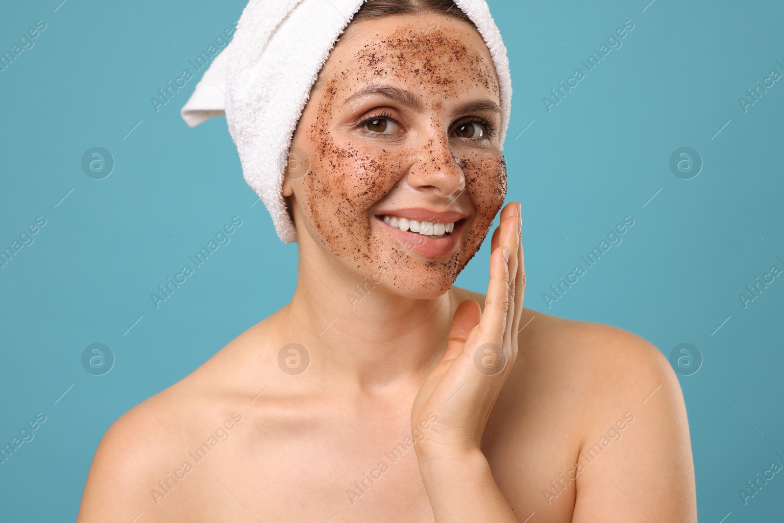 Smiling woman with body scrub on her face against light blue background Photo of Smiling woman with body scrub on her face against light blue background