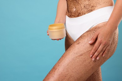 Photo of Woman with body scrub on her skin and jar against light blue background, closeup. Space for text
