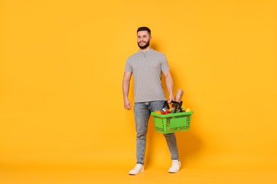 Photo of Man with shopping basket full of products on orange background