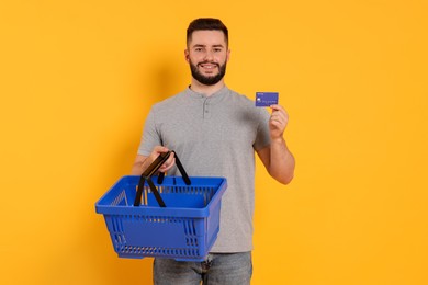 Photo of Man with empty shopping basket and credit card on orange background