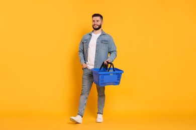 Photo of Man with empty shopping basket on orange background